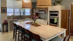 Una cocina moderna con una isla grande, dos lámparas colgantes de mimbre y electrodomésticos integrados.