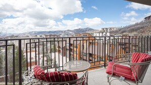 A balcony with a view of a mountainous landscape, a table, and two chairs with striped cushions. - BT301 | Mountainside Condo | Great views | Winter Shuttle | Ski In | Hot Tub (Steamboat Springs)