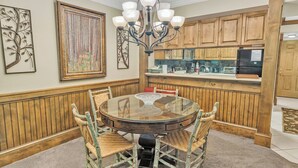 A dining area with a round glass table, wooden chairs, a chandelier, and wooden paneling on the walls. - Beautiful two bedroom condo that sleeps 4 (Gatlinburg)