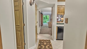 A hallway with a wooden door, a light fixture, a kitchen area with cabinets and a dishwasher, and a view of a patio. - Beautiful two bedroom condo that sleeps 4 (Gatlinburg)