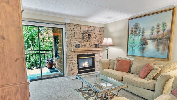 A living room with a stone fireplace, a glass coffee table, a beige sofa, and a painting of a landscape. - Beautiful two bedroom condo that sleeps 4 (Gatlinburg)