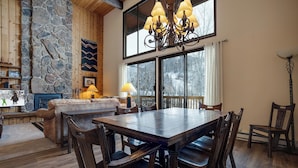 A spacious dining area with a large wooden table and chairs, a stone accent wall, and a view of a snowy landscape through large windows.
