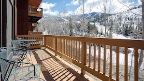 A wooden deck with metal chairs, overlooking a snowy mountain landscape.