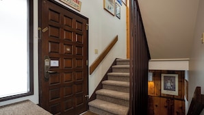 A wooden door with a brass handle, a carpeted staircase with a wooden handrail, and a framed picture on the wall.