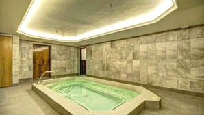 Uma piscina interior moderna, com formato retangular, rodeada por paredes de mármore e chão ladrilhado.