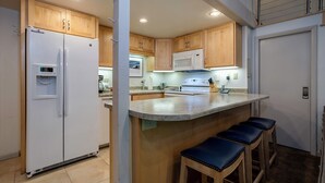A kitchen with wooden cabinets, a white refrigerator, a microwave, and a stove. There are two bar stools and a water dispenser.