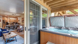 A spacious living area with a sliding glass door leading to a hot tub, wooden flooring, and a dining area with a table and chairs. - Managed by Park City Lodging-Deluxe Condo Walk to Town Lift and Main Street (PARK CITY)