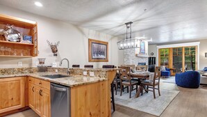 A kitchen with wooden cabinets, a dishwasher, granite countertops, and a dining area with a table and chairs. - Managed by Park City Lodging-Deluxe Condo Walk to Town Lift and Main Street (PARK CITY)