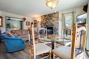 A cozy living room with a stone fireplace, a glass dining table, and comfortable seating. - SC100 | Walk-Out Patio | Hot Tub | Steps Away from Skiing (Steamboat Springs)