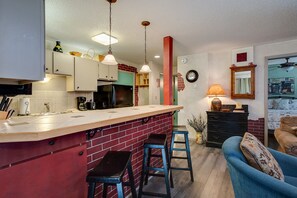 A kitchen with a red brick backsplash, a wooden island, and blue bar stools. There is a black refrigerator, a sink, and a coffee maker on the counter. - SC100 | Walk-Out Patio | Hot Tub | Steps Away from Skiing (Steamboat Springs)