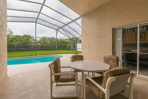 A covered patio with a pool, outdoor furniture, and a view of greenery.