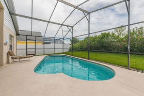 A swimming pool with a glass enclosure, a lounge chair, and a house in the background.