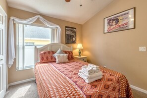 A bedroom with a bed, pillows, a nightstand, a lamp, a window with curtains, and a poster on the wall.