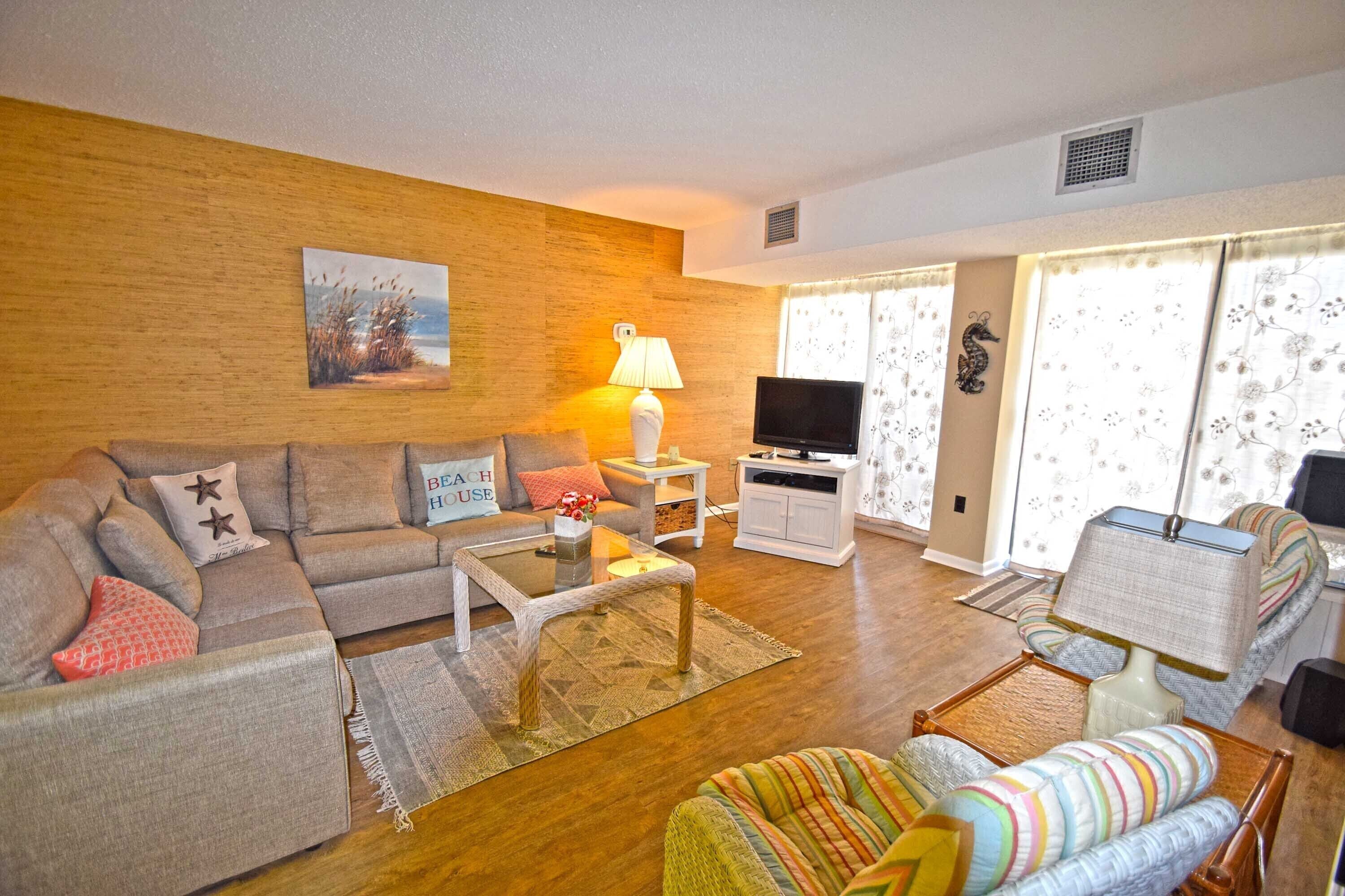 A living room with a sofa, a coffee table, a TV, and a window with curtains.
