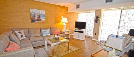 A living room with a sofa, a coffee table, a TV, and a window with curtains.