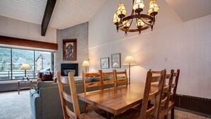 A dining area with a wooden table and chairs, a fireplace, and a chandelier. - GSQ32 | Nice Views | Huge Private Deck | Steps from Steamboat Square (Steamboat Springs)