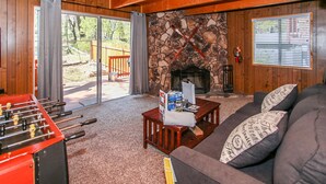 A cozy living room with a stone fireplace, a foosball table, and a sofa with patterned cushions.