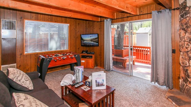 A cozy living room with a foosball table, a sofa, and a coffee table with books and a remote control.