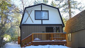 A cabin with a wooden deck, a large window, and a door.