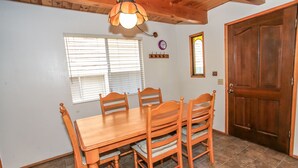A dining room with a wooden table and chairs, a window with blinds, a clock, and a door.