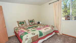 A bedroom with a large bed, a window with curtains, and a view of trees outside.