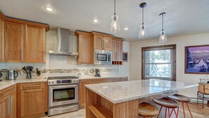 Une cuisine moderne avec des meubles en bois, des appareils en acier inoxydable, un grand îlot central doté de tabourets et un éclairage suspendu.