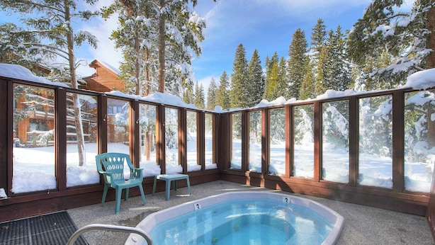 Une piscine extérieure chauffée, avec vue sur des arbres couverts de neige et un chalet en bois en arrière-plan.
