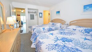 Habitación de hotel con dos camas, un tocador, una lámpara y una puerta que da a otra habitación.