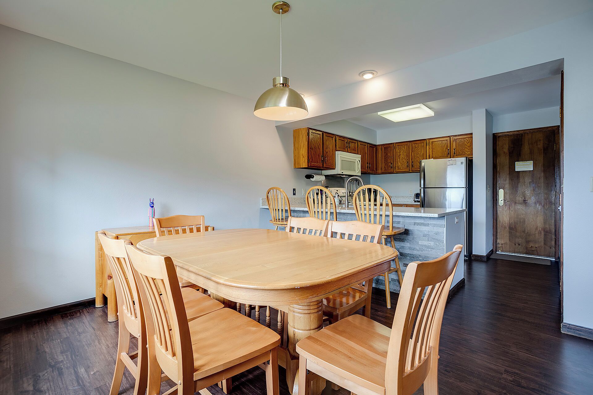 A dining area with a wooden table and chairs, a kitchen with wooden cabinets and appliances, and a door with a sign.