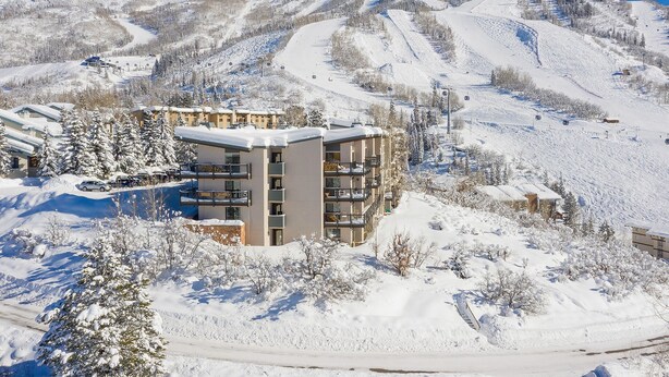 A multi-story hotel with balconies, surrounded by snow-covered trees and mountains.