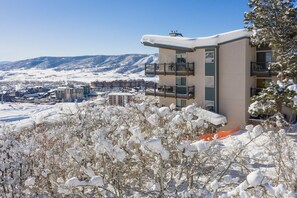Un edificio de varios pisos con balcones, rodeado de árboles cubiertos de nieve y un paisaje montañoso al fondo.