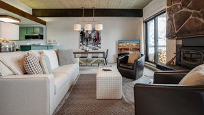 A cozy living room with a fireplace, a dining area, and a kitchen in the background.