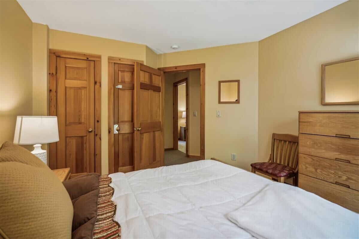 A bedroom with a bed, a dresser, a chair, and two wooden doors.