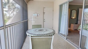 A balcony with a small table, a door, and a sliding glass door leading to a room.