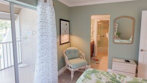 A bedroom with a bed, a chair, a dresser, a mirror, and a shower area.