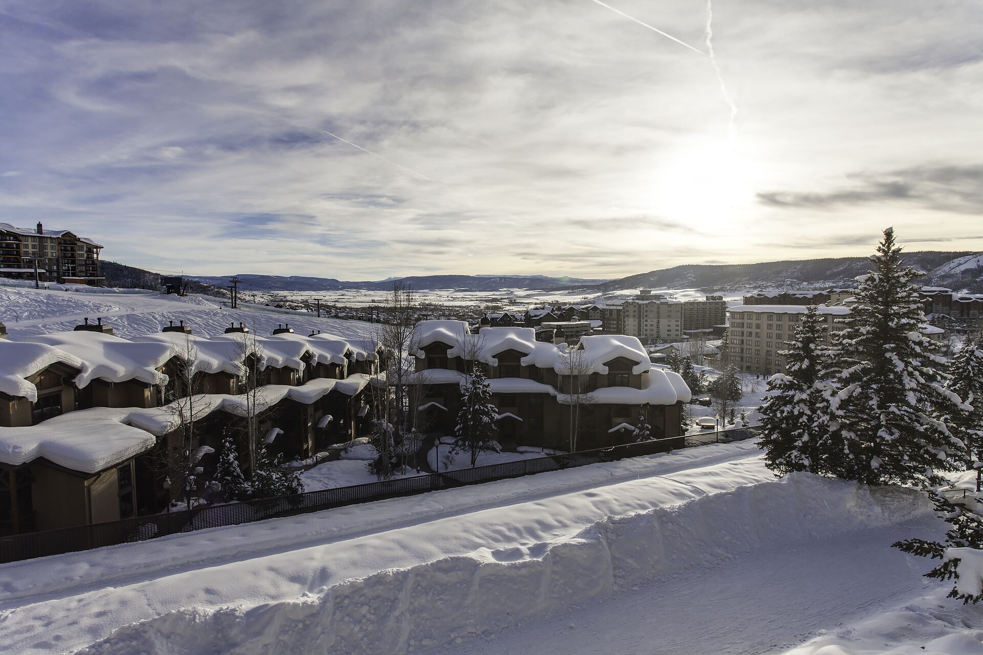 Une station de ski enneigée, avec plusieurs bâtiments de style chalet, une piste de ski et un paysage montagneux en toile de fond.