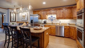 A modern kitchen with wooden cabinets, stainless steel appliances, and a central island with bar stools. - HM3E | Pure luxury | A/C | Hot Tub | Pool | Steps from Mtn Village (Steamboat Springs)