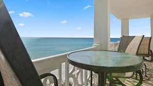 Un balcone con tavolo e sedie in vetro, vista su un mare cristallino e azzurro.
