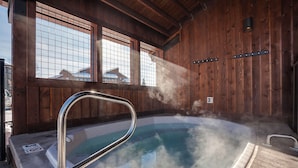 A hot tub with a metal railing, steam rising from the water, and wooden walls with a window in the background.