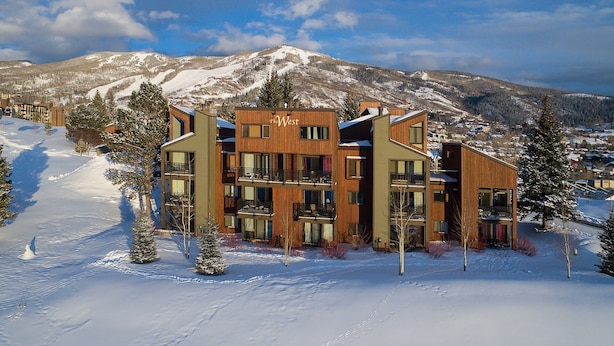 A modern multi-story hotel with a ski resort backdrop, featuring balconies and large windows.