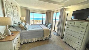 A bedroom with a large bed, a dresser, a television, and a view of the ocean. - Festive, fun 2 bedroom oceanfront condo with free WiFi, unique and sunny decor, and a beautiful view of the ocean located in quiet midtown and just a few steps to the beach! (Ocean city)
