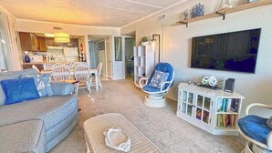 A living room with a sofa, chairs, a small table, a bookshelf, and a television. - Festive, fun 2 bedroom oceanfront condo with free WiFi, unique and sunny decor, and a beautiful view of the ocean located in quiet midtown and just a few steps to the beach! (Ocean city)