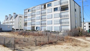 A multi-story building with balconies, a sandy foreground, and a clear sky. - Festive, fun 2 bedroom oceanfront condo with free WiFi, unique and sunny decor, and a beautiful view of the ocean located in quiet midtown and just a few steps to the beach! (Ocean city)