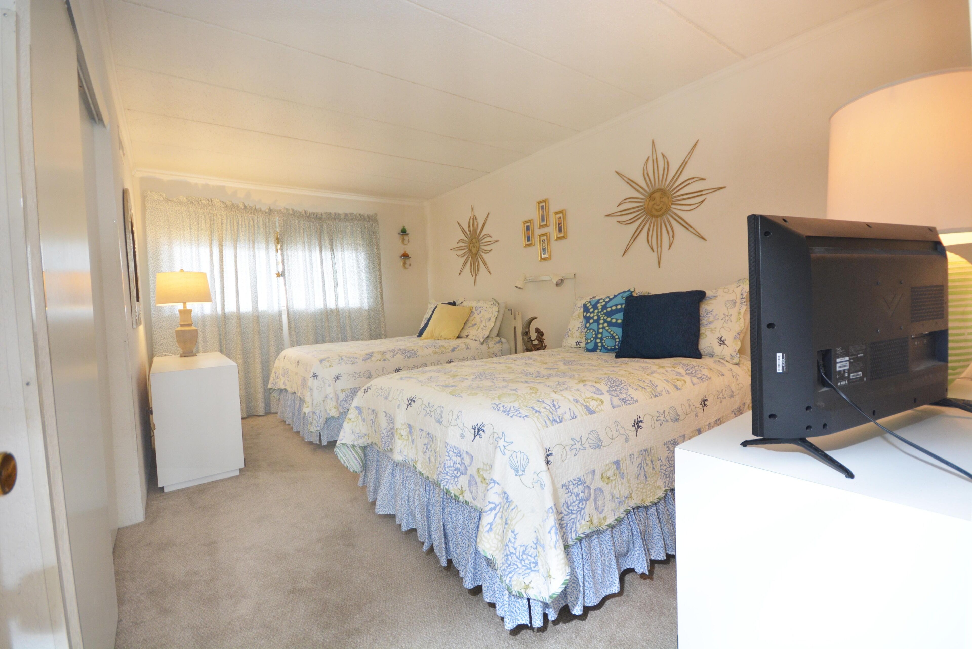 Une chambre avec deux lits, une télévision et une petite armoire blanche.