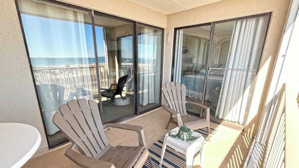 A balcony with two chairs, a small table, and a view of the ocean. - Festive, fun 2 bedroom oceanfront condo with free WiFi, unique and sunny decor, and a beautiful view of the ocean located in quiet midtown and just a few steps to the beach! (Ocean city)