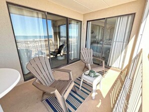 A balcony with two chairs, a small table, and a view of the ocean. - Festive, fun 2 bedroom oceanfront condo with free WiFi, unique and sunny decor, and a beautiful view of the ocean located in quiet midtown and just a few steps to the beach! (Ocean city)