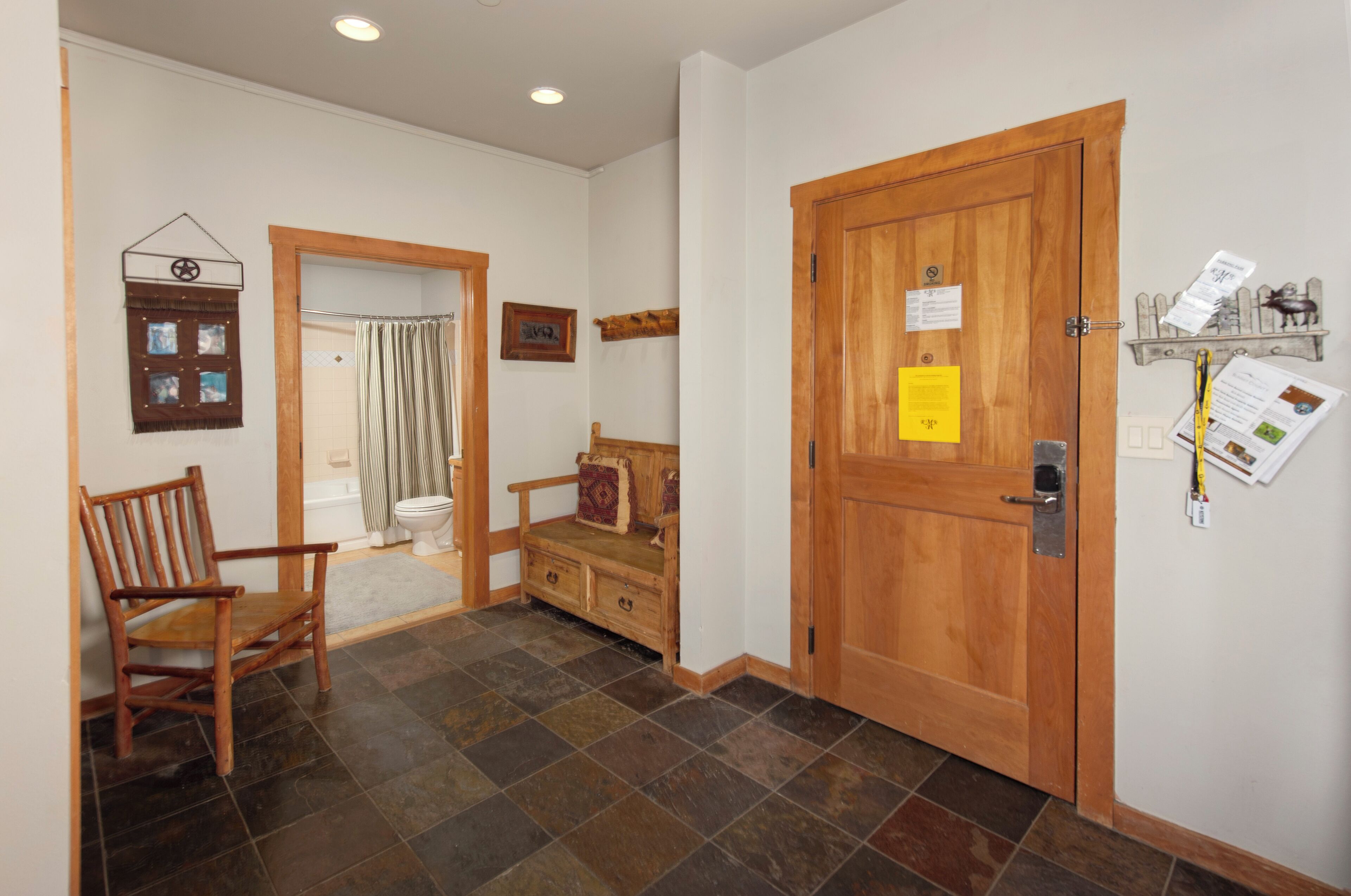 A hallway with a wooden door, a bench, a chair, and a small table.