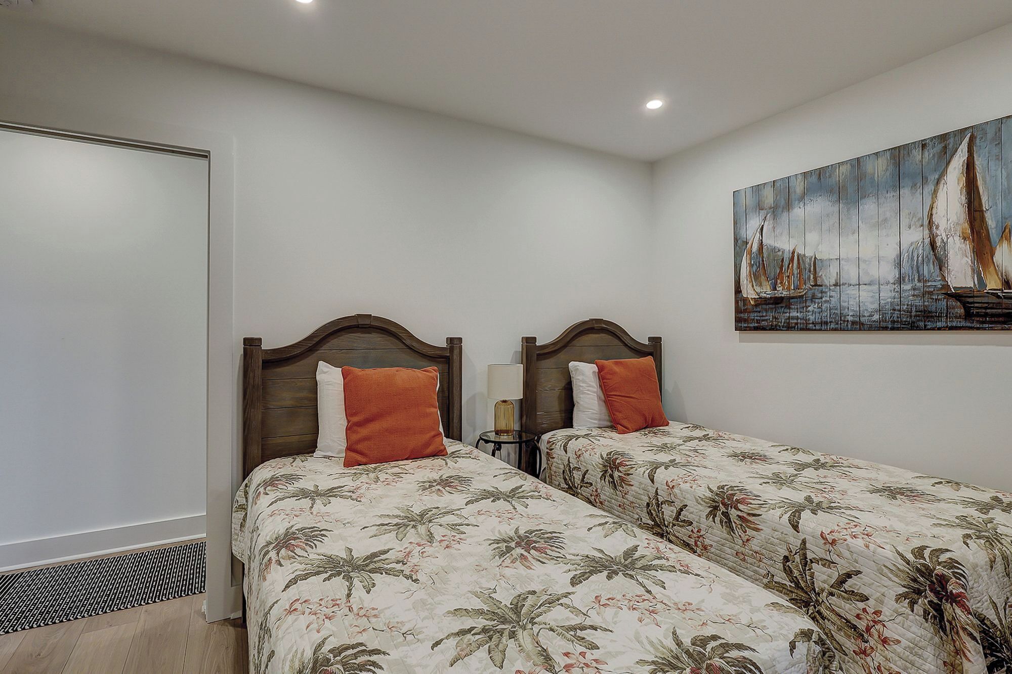 Quarto com duas camas, cada uma com cabeceira de madeira e roupa de cama floral. Há um quadro de um veleiro na parede.