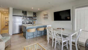 A modern kitchen with a central island, bar stools, and a dining area with white chairs. - Oceanfront Villa, Heated Beachside Pool! (Hilton Head)