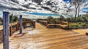 A wooden deck with benches and a hose, leading to a view of the ocean under a cloudy sky. - Oceanfront Villa, Heated Beachside Pool! (Hilton Head)